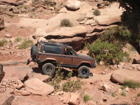 1986 Ford Bronco II - Brown 1986 Ford Bronco II tackles a challenging off-road path in a desert landscape.