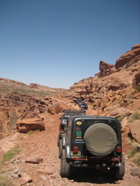 1986 Ford Bronco II - A line of Jeeps navigates a challenging off-road path through a desert landscape under a clear blue sky.