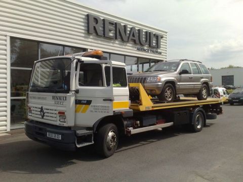 1991 Ford LTD Crown Victoria - A Jeep Grand Cherokee is being towed by a Renault tow truck in front of a dealership.