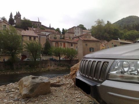 1991 Ford LTD Crown Victoria - Close-up of a silver Jeep Grand Cherokee's front grille and headlight, with a scenic European village and river in the background.