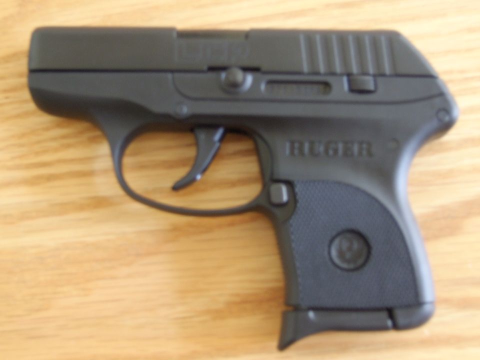 Black Ruger LCP pistol on wooden surface. Text on slide reads LCP and RUGER. Supermotors.net logo in corner