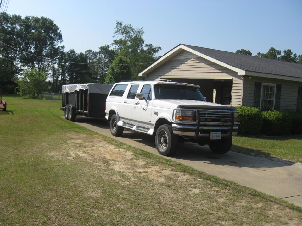 White Ford Bronco SUV towing a covered utility trailer in a driveway