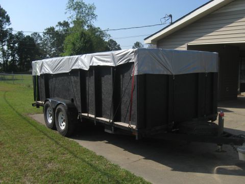 1995 Ford C-350 (Centurion Conversions) - A black trailer with a silver tarp is parked on a concrete driveway beside a house.