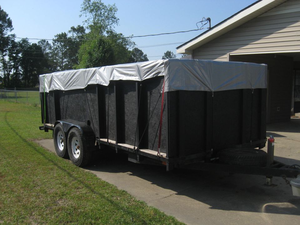 Black trailer with a silver tarp covering the top, parked on a driveway next to a house