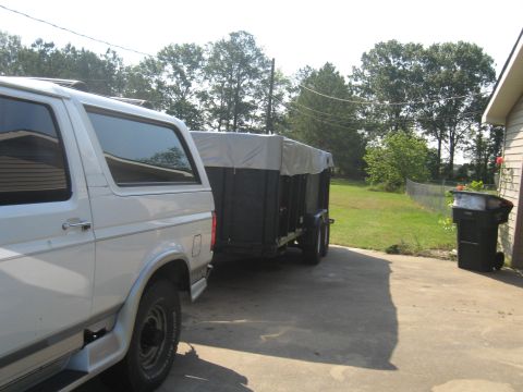 1995 Ford C-350 (Centurion Conversions) - A white SUV is parked beside a covered trailer, with a trash can and house in the background.