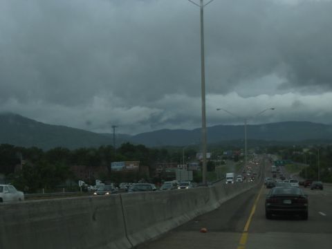 1995 Ford C-350 (Centurion Conversions) - Traffic moves along a highway with mountains visible in the distance under a cloudy sky.