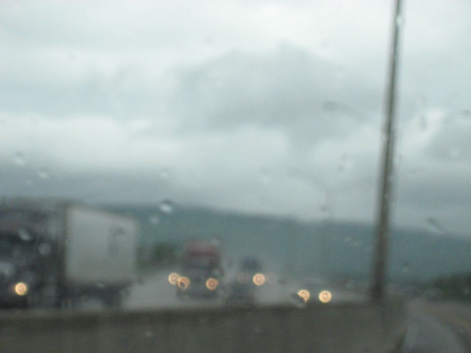 Trucks on a wet highway under a cloudy sky, viewed through a rain-streaked windshield