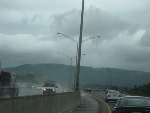 1995 Ford C-350 (Centurion Conversions) - Vehicles navigate a wet highway under cloudy skies, with a mountain range visible in the distance.