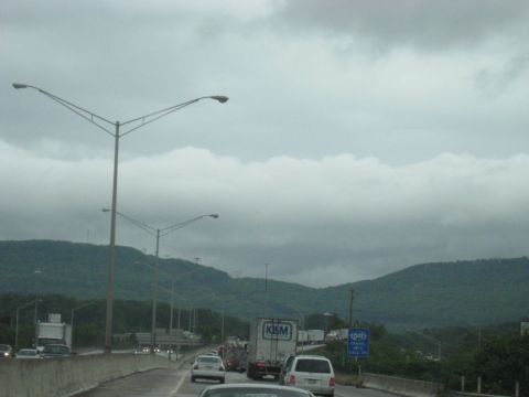 1995 Ford C-350 (Centurion Conversions) - Traffic is backed up on a highway with mountains visible in the distance under a cloudy sky.