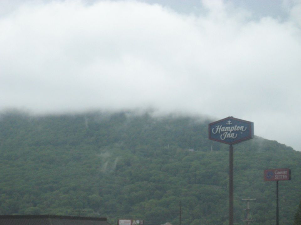 Hampton Inn sign in front of a tree-covered mountain with clouds