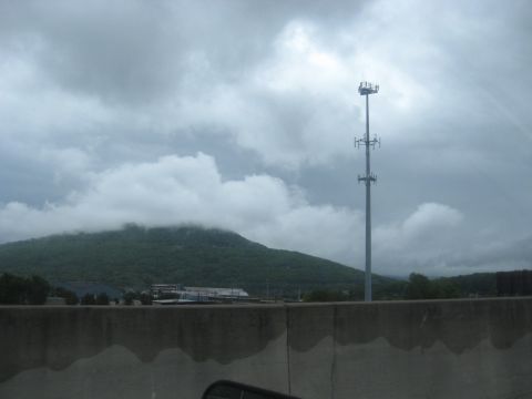 1995 Ford C-350 (Centurion Conversions) - A cell tower stands tall against a backdrop of a cloud-shrouded mountain and a gray sky.