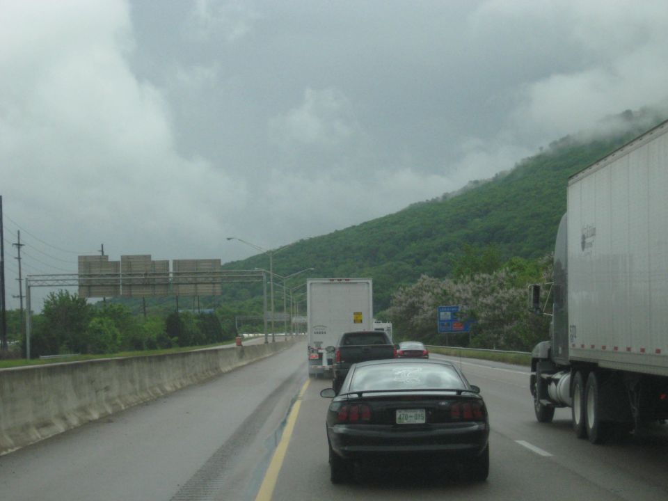 Highway traffic scene with trucks and cars on a cloudy day, green mountain in background