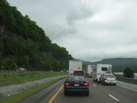 1995 Ford C-350 (Centurion Conversions) - Vehicles are stopped in traffic on a highway with a mountain on the left and water on the right.