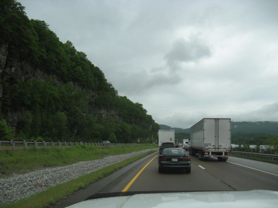 Traffic on a highway with a cliff face and trees on the left