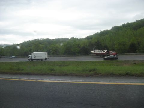 1995 Ford C-350 (Centurion Conversions) - A truck transports a boat on a highway under an overcast sky.