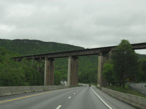 1995 Ford C-350 (Centurion Conversions) - A long railroad bridge supported by concrete pillars spans over a highway on a cloudy day.