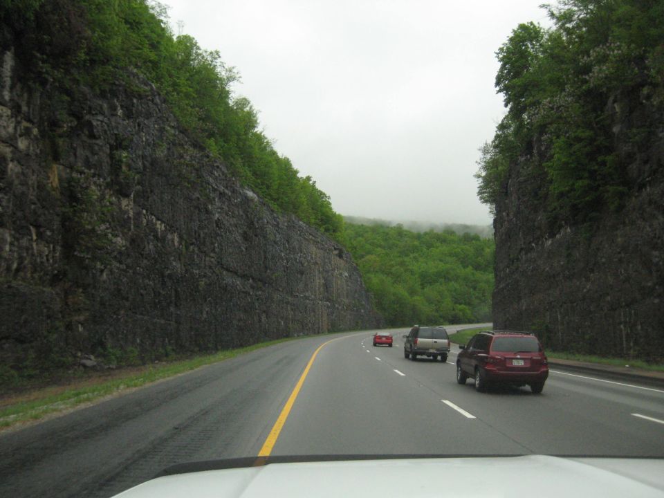 Highway scene with vehicles driving between rock cliffs and green trees