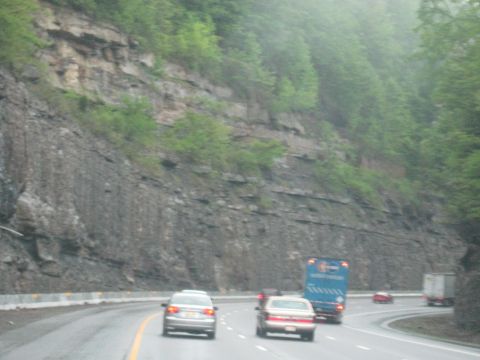 1995 Ford C-350 (Centurion Conversions) - Vehicles travel along a highway bordered by a steep, rocky embankment covered in greenery.