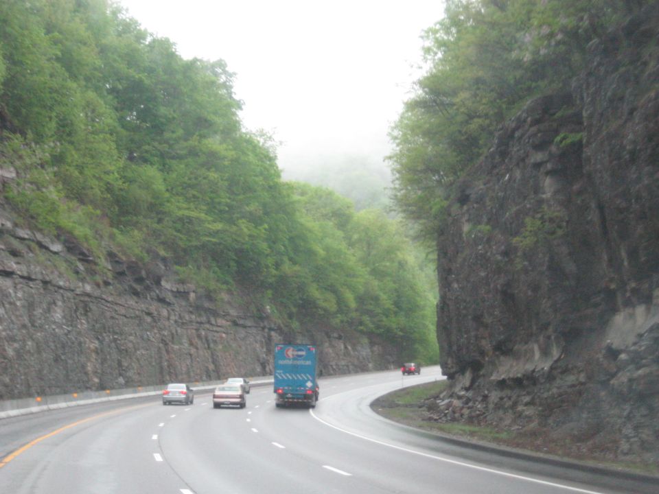 Blue truck on a wet highway with rocky cliffs and trees