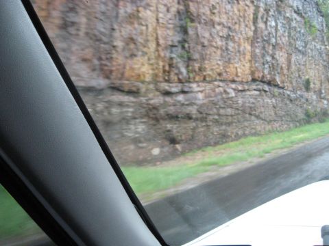 1995 Ford C-350 (Centurion Conversions) - Driving past a large rock cliff face alongside a road.