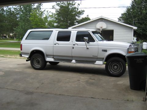 1995 Ford C-350 (Centurion Conversions) - White extended cab pickup truck with a camper shell, side view, parked on concrete. Visible text on trash can.
