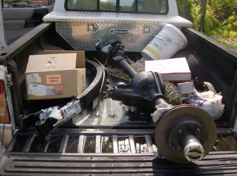 1989 Ford Bronco - Various automotive parts, including a rear axle assembly and leaf springs, are stored in the bed of a pickup truck.