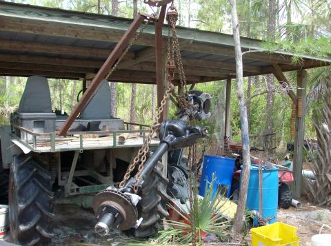 1989 Ford Bronco - A heavy-duty axle assembly is suspended by a crane, with a large tractor tire nearby.