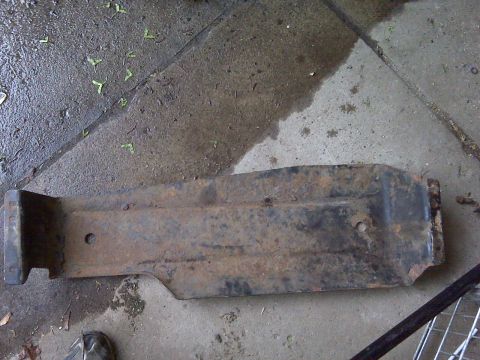 1995 Ford Bronco - This is a rusty metal part lying on a wet concrete surface with some leaves scattered around.