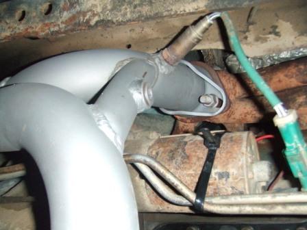 1996 Ford Bronco - Underbody shot of a freshly fabricated aluminized exhaust downpipe with a mandrel bend and a welded bung holding an oxygen sensor. Behind i…