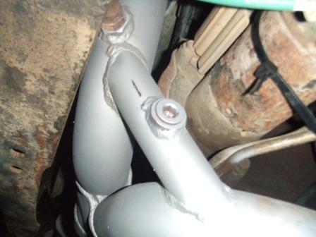 1996 Ford Bronco - Close-up of an exhaust pipe assembly, showing welded joints and fasteners, with hints of the vehicle's undercarriage.