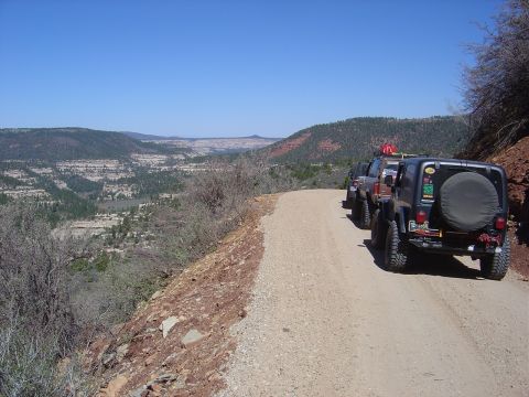 1986 Ford Bronco II - Off-road vehicles parked on a dirt road with a scenic canyon view.