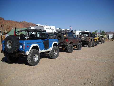 1986 Ford Bronco II - Several modified SUVs are parked in a line on a dirt road under a clear blue sky.