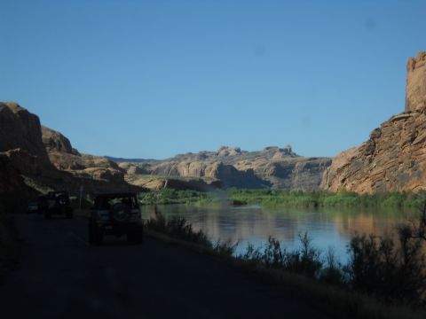 1986 Ford Bronco II - Off-road vehicles travel along a river in a canyon landscape under a clear blue sky.