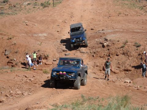 1986 Ford Bronco II - Two SUVs navigate a challenging dirt road in a dry, arid environment.