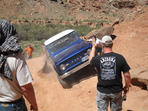 1986 Ford Bronco II - A blue Ford Bronco navigates a steep, rocky trail with onlookers present.