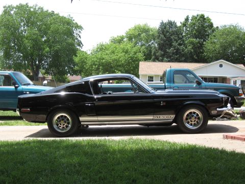 1968 Shelby GT500 - A black 1968 Shelby GT500KR is parked on a driveway next to a teal pickup truck.