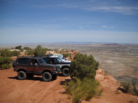 1986 Ford Bronco II - Three SUVs, including a 1986 Ford Bronco II, are parked on a cliff edge with a scenic desert view.