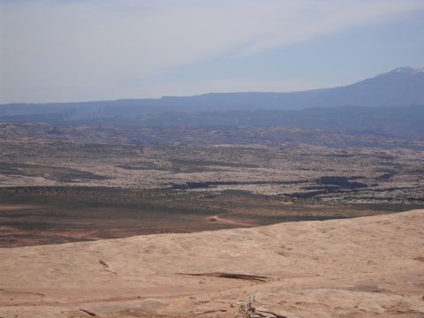 1986 Ford Bronco II - A vast desert landscape unfolds under a hazy sky, with mountains on the horizon and a dirt road visible in the distance.