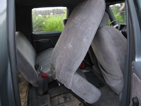 1986 Ford Bronco - The interior of a vehicle shows gray fabric seats and the floor, with a red object visible.