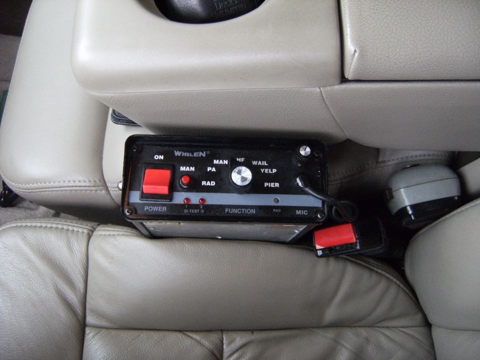 Emergency equipment control box with red buttons and labels like 'POWER' and 'FUNCTION' mounted between tan leather seats