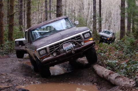 1979 Ford Bronco - Two Ford trucks navigate a challenging off-road course through a wooded area.