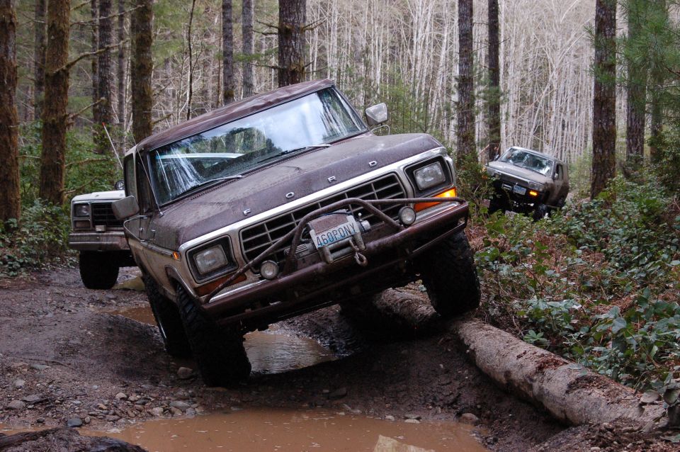 Muddy brown Ford truck with tube bumper climbing a log on a forest mud trail