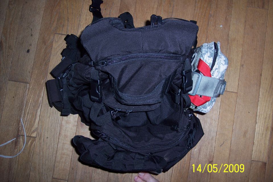 Black tactical backpack with camo pouch on hardwood floor, dated 14/05/2009
