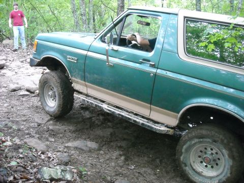 1979 Ford F-150 - Ford Bronco navigates a rough, wooded trail with a driver and passenger visible.