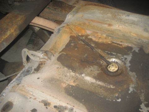 1983 Ford F-250 - Close-up view of a heavily rusted fuel tank, showing hoses and the sender unit, with parts of the vehicle's frame visible.
