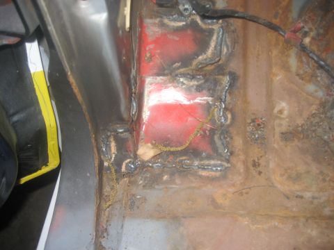 1983 Ford F-250 - Close-up view of a rusted and repaired metal floor pan, showing welding marks and red undercoating.