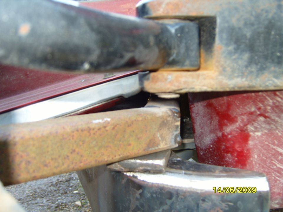 Rusty metal bracket attached to a red vehicle's rear bumper area