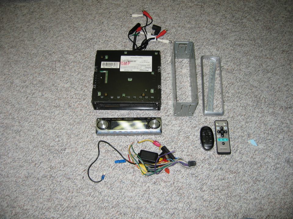 Pioneer car stereo head unit disassembled with mounting sleeve, wiring harness and remote on carpet