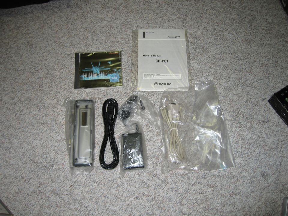 Car stereo components including a faceplate, cables, and owner's manual on carpet