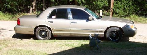 2000 Mercury Grand Marquis - A tan sedan is parked on a grassy area with trees in the background.
